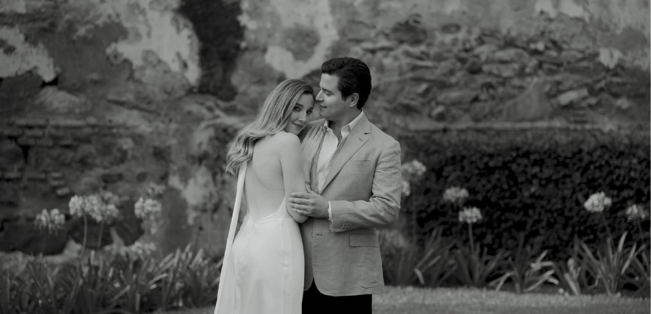 Black and white portrait of bride and groom embracing by a stone wall