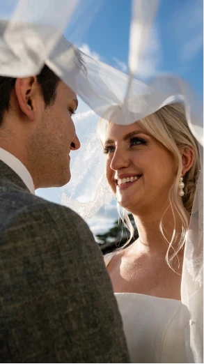 Bride and groom smiling under the veil against a blue sky